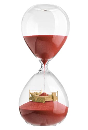 An hourglass with sand falling to the bottom, pilling on top of a mattress.