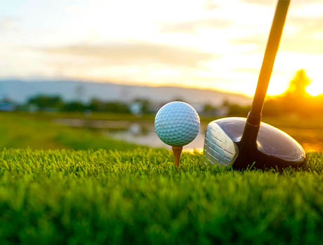 Golf ball on tee next to a driver club at sunset on a lush green golf course.