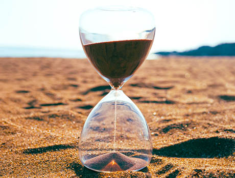 An hourglass with flowing sand on a beach.