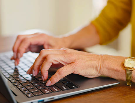 Hands typing on a laptop keyboard in a home office setting.