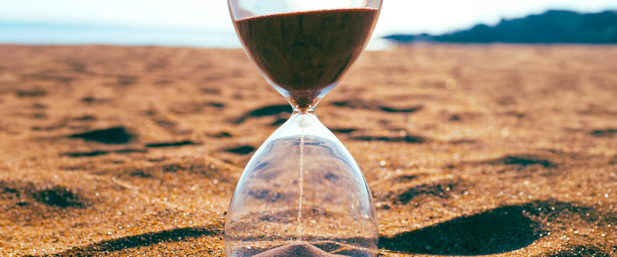 An hourglass with flowing sand on a beach. An hourglass with flowing sand on a beach.